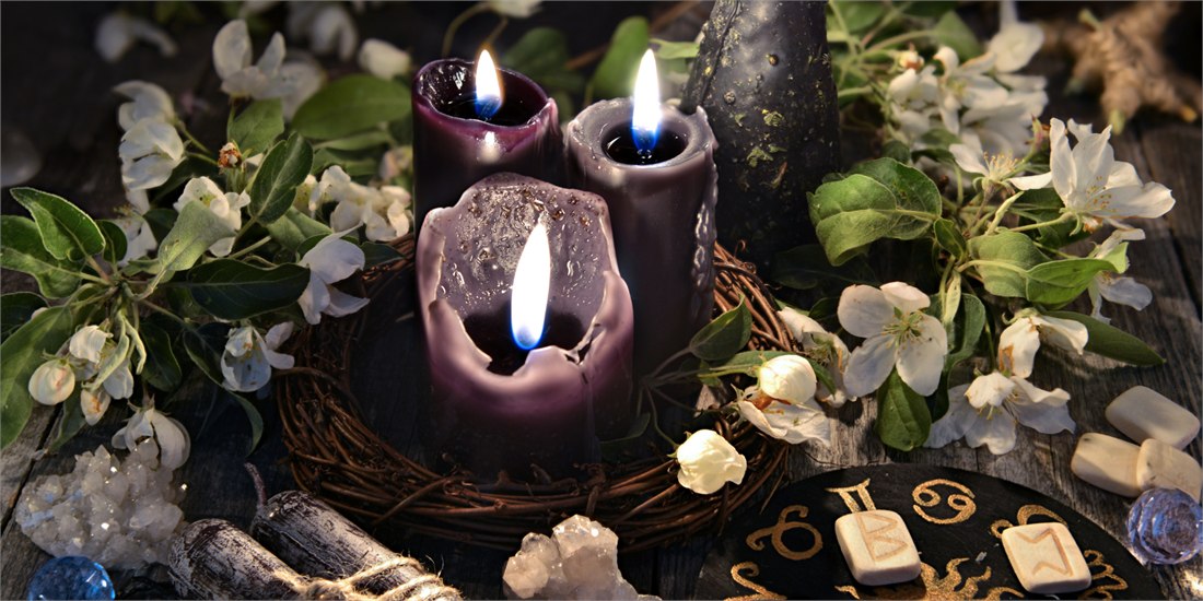 Candele viola accese tra fiori bianchi, cristalli e rune: l’altare rituale del Passaggio per l’Eternità